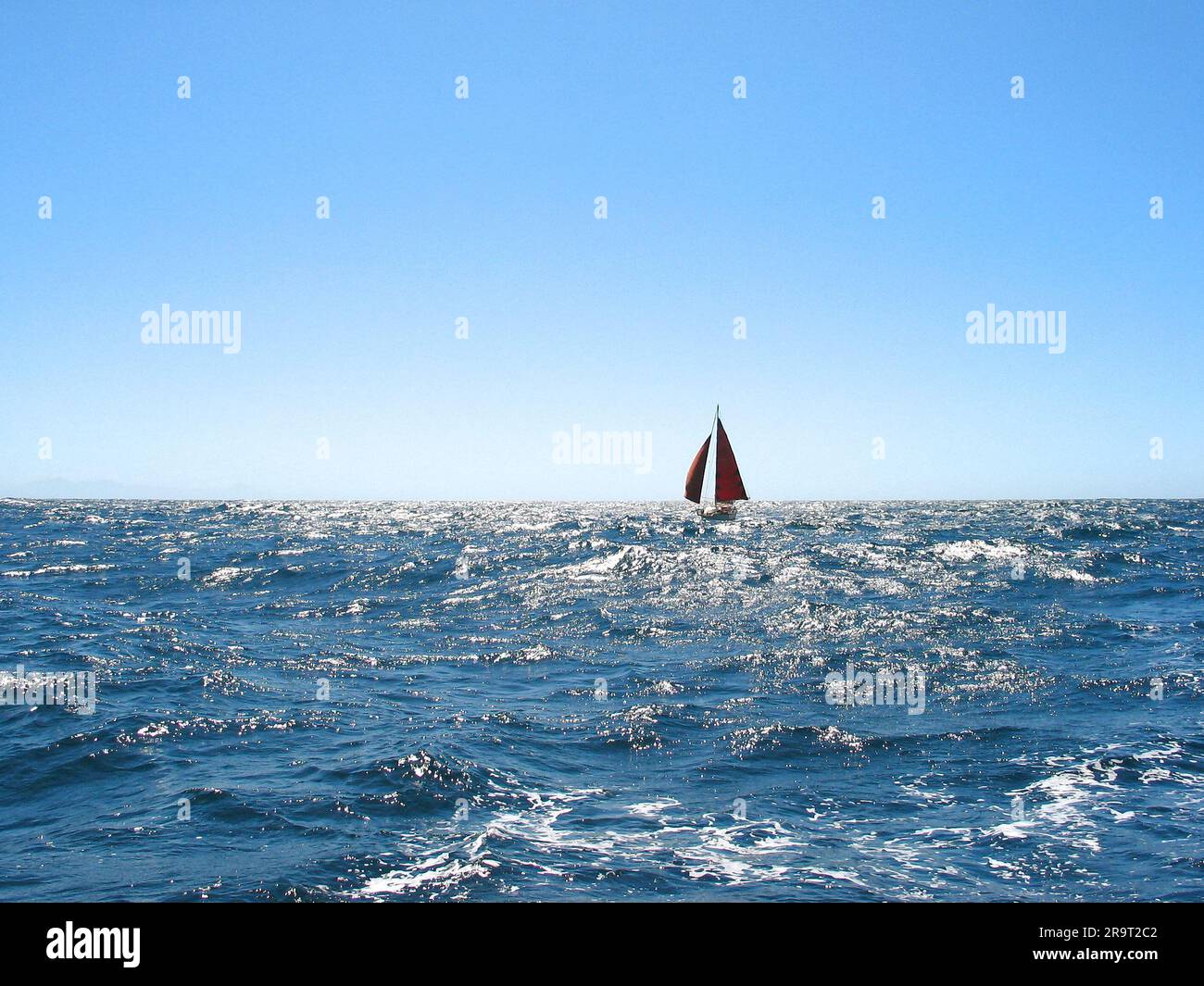 Silhouette of a small sailing boat on the horizon, blue ocean and perfect trade wind day at sea. Stock Photo