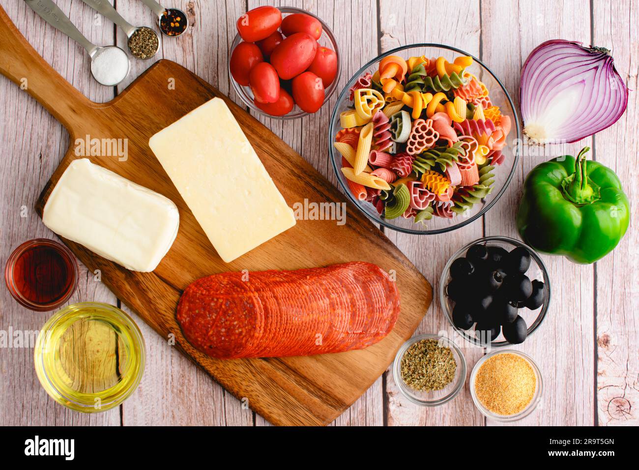 Classic Pasta Salad Ingredients on a Light Wooden Background: Uncooked pasta, olive oil, cheeses, and more on a rustic background Stock Photo
