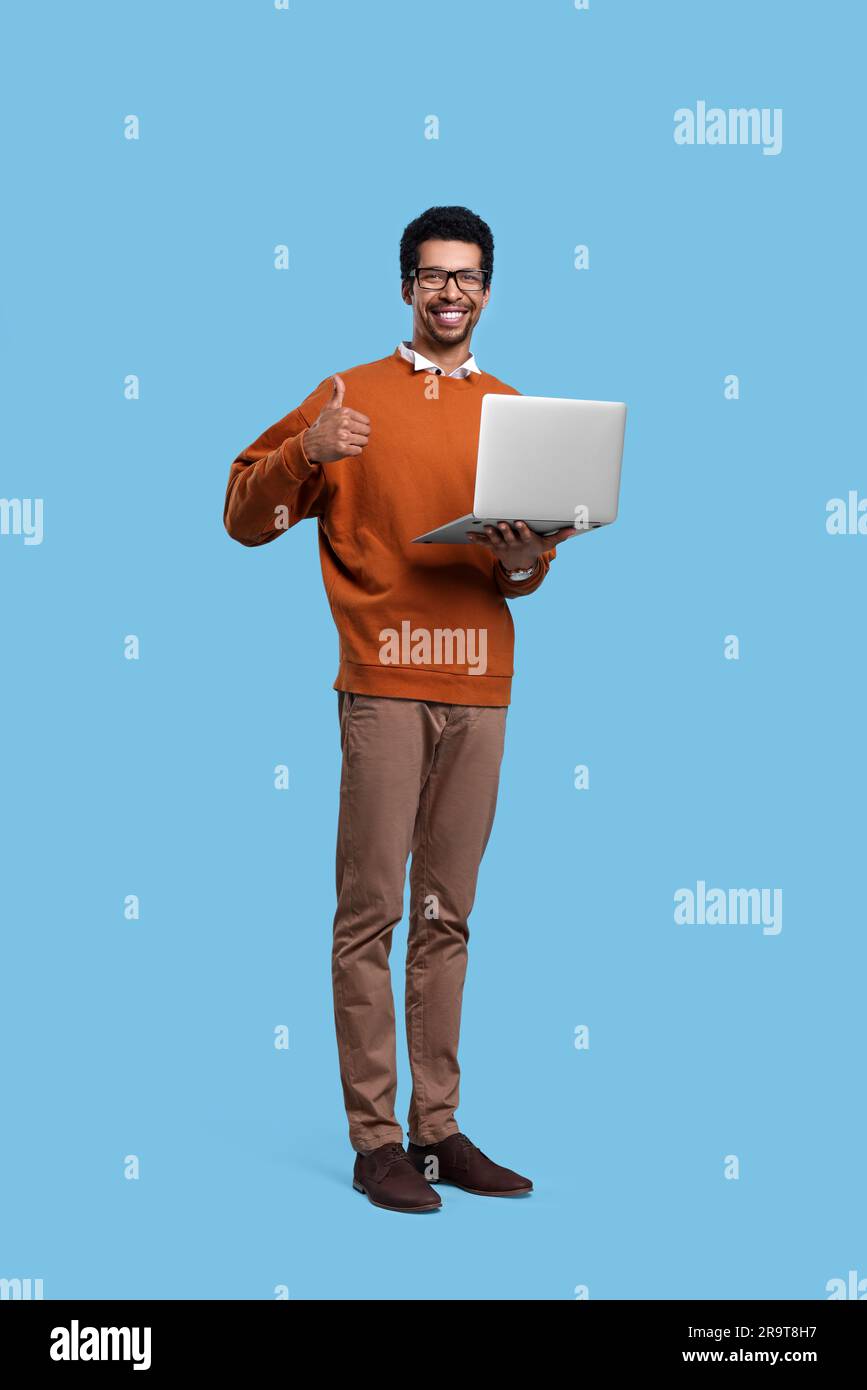 Happy man with laptop showing thumb up on light blue background Stock ...