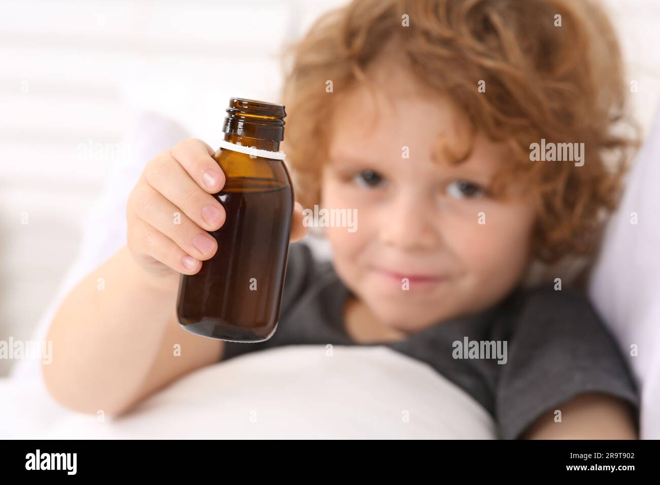 Cute boy holding cough syrup in bed, focus on bottle Stock Photo Alamy