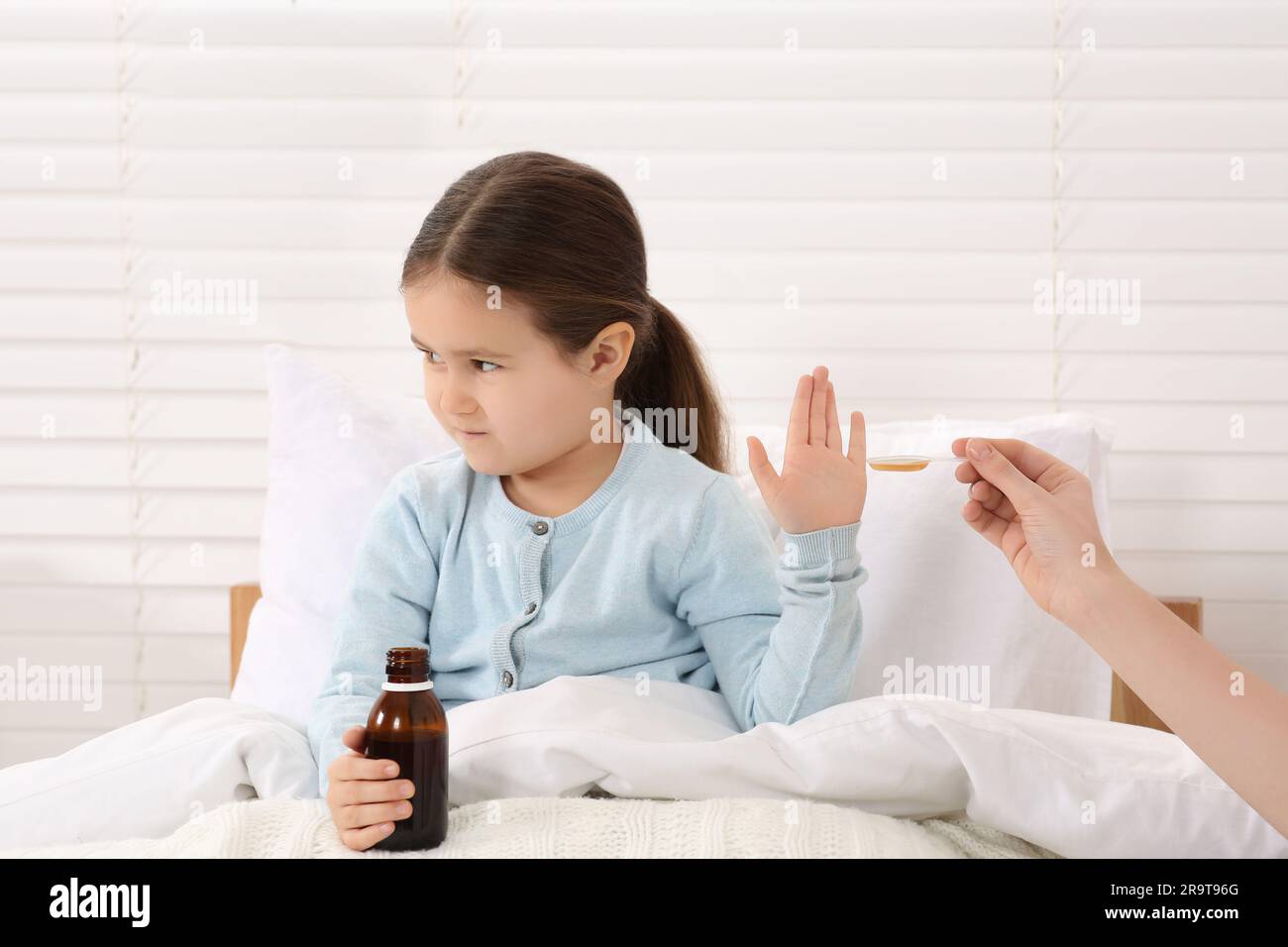 Daughter refusing to take cough syrup from her mother in bedroom Stock