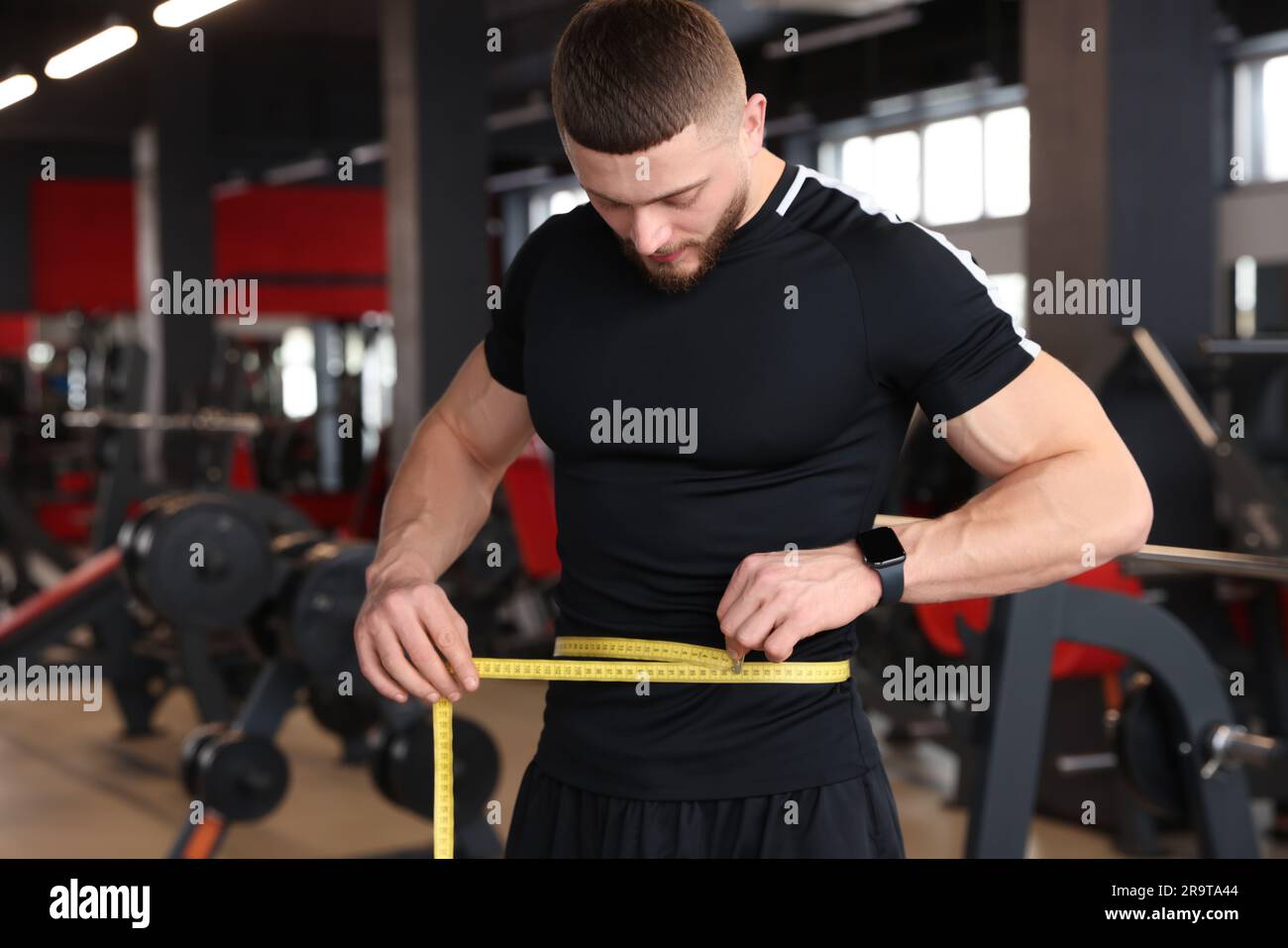 Athletic man measuring waist with tape in gym Stock Photo