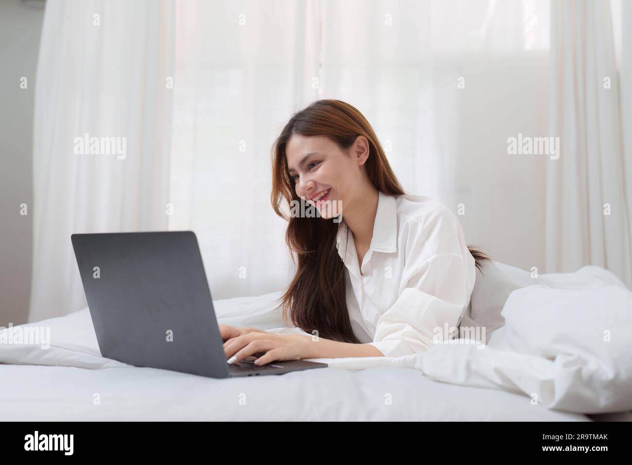 Happy smiling asian woman stretching on bed in the morning and using ...