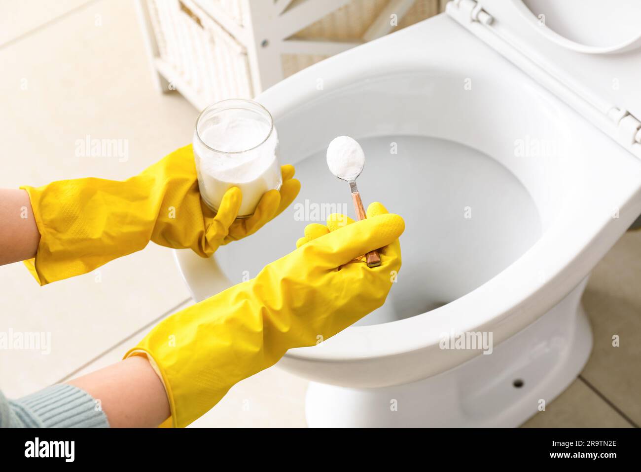 Woman in rubber gloves cleaning toilet bowl with baking soda Stock