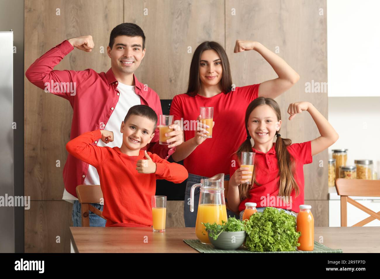 Happy family with orange juice showing muscles in kitchen Stock Photo