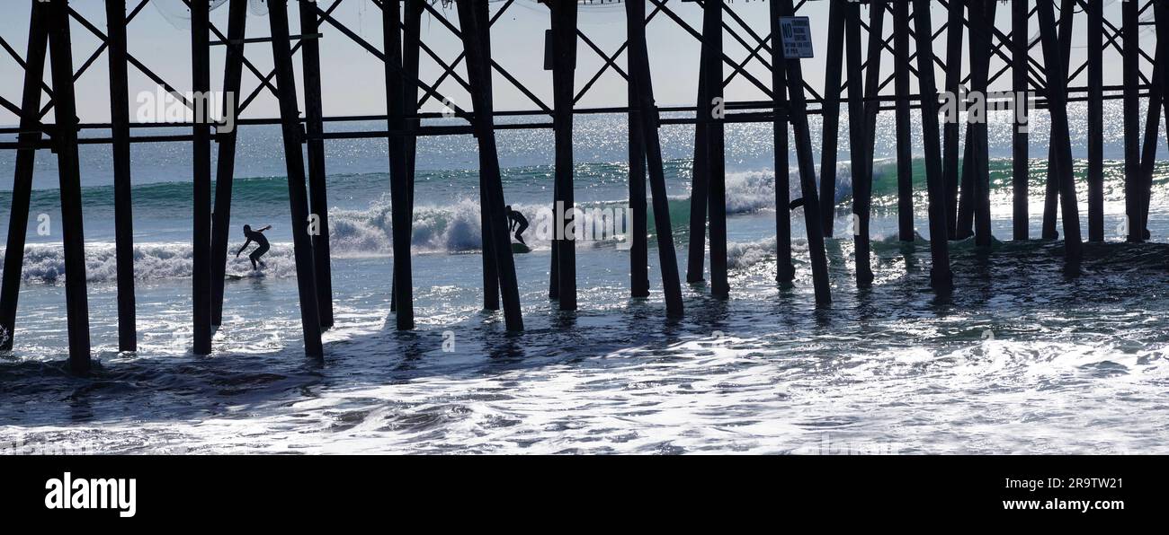 Surfers surfing by pier at Oceanside, California, USA Stock Photo