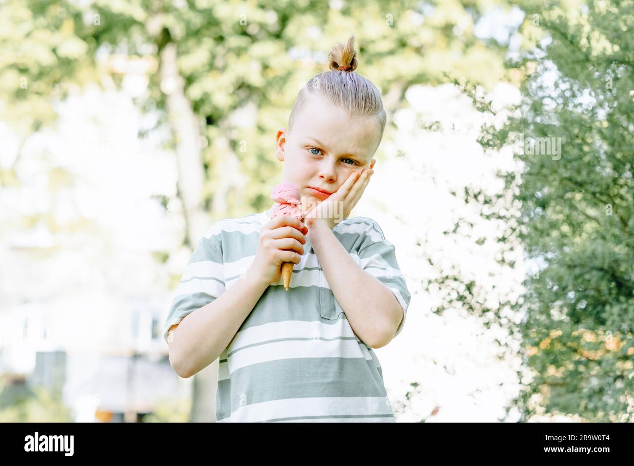 Sad child clutched his cheek with his hand and held an ice cream cone in his other hand. Problems sensitivity of teeth in a child or tooth decay. Stock Photo