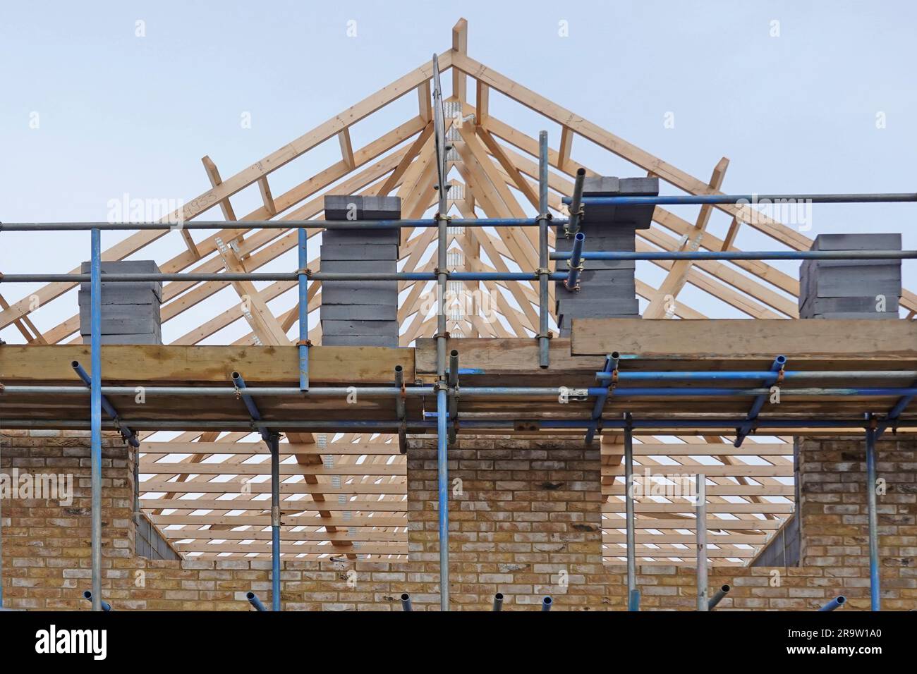 Factory prefabricated timber roof trusses on detached house building construction site in position scaffold loaded blocks gable end wall England UK Stock Photo