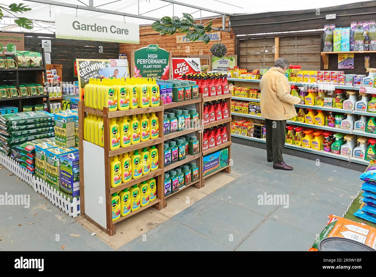 Mature woman gardener selecting hand held weed control spray on chemical at Garden Care shelves at horticulture gardening nursery business England UK Stock Photo