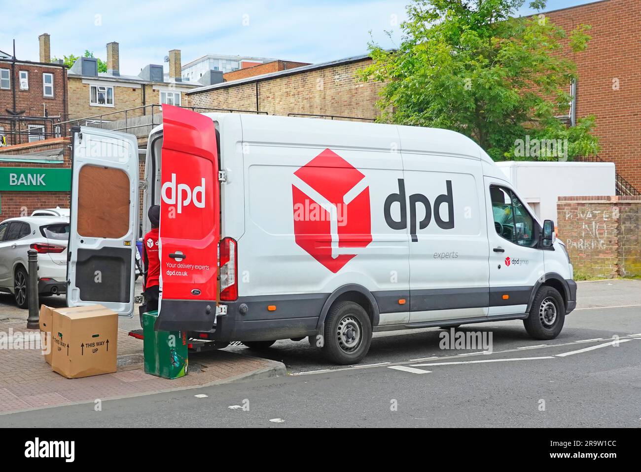 Side back view rear open doors of red white DPD parcel delivery van driver sorting parcels high street retail businesses via back entrances England UK Stock Photo