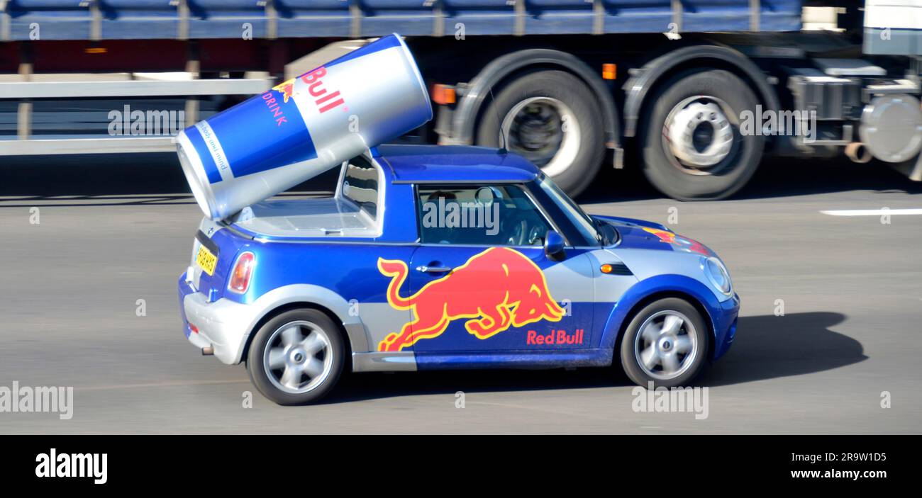 Customised advertising Red Bull brand energy drink by incorporating large can & logo into mini car body driving on M25 motorway road Essex England UK Stock Photo