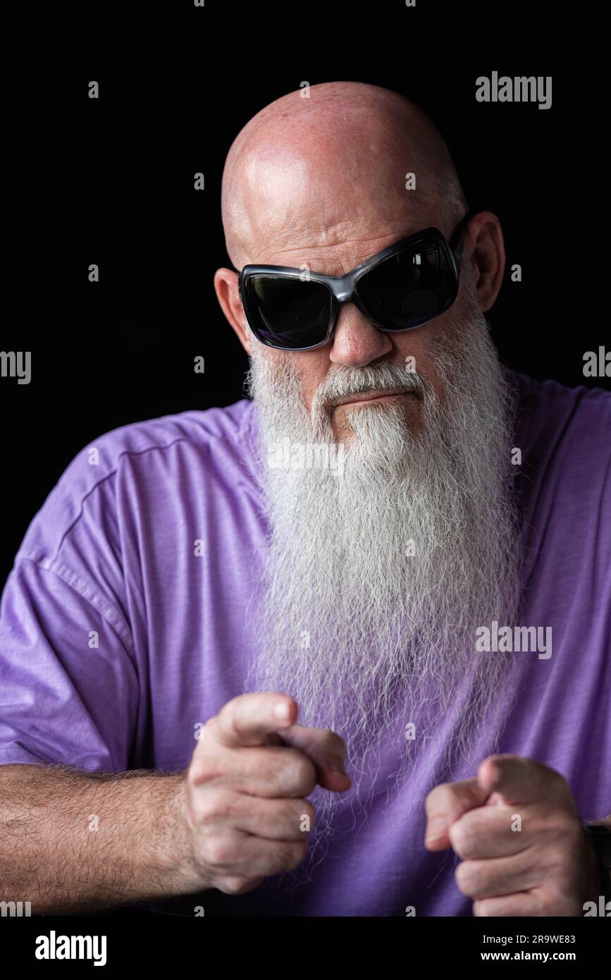 Portrait of man with long gray beard wearing purple t-shirt and sunglasses showing fingers to camera Stock Photo