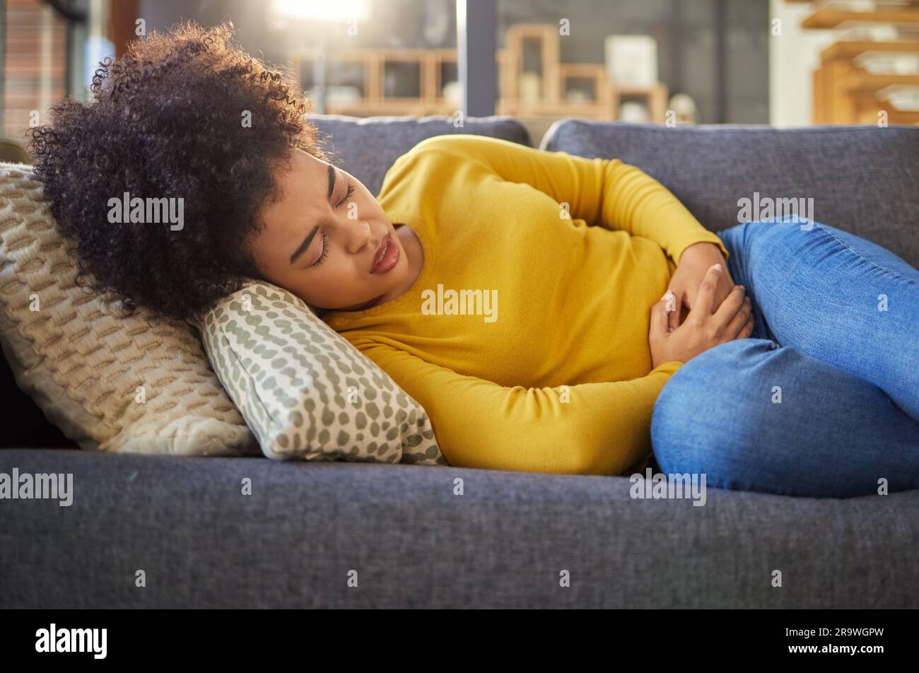 Stomach pain, sick and menstruation with woman on sofa for healthcare