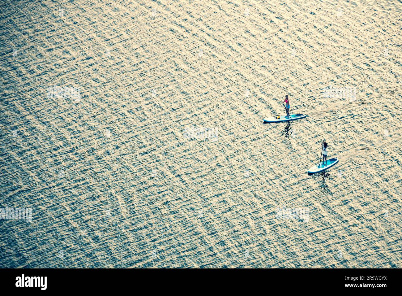Two paddleboarders girls boarding or floating on a stand up paddle on the quite water of a lake with warm summer sunset colours, water sport, aerial Stock Photo