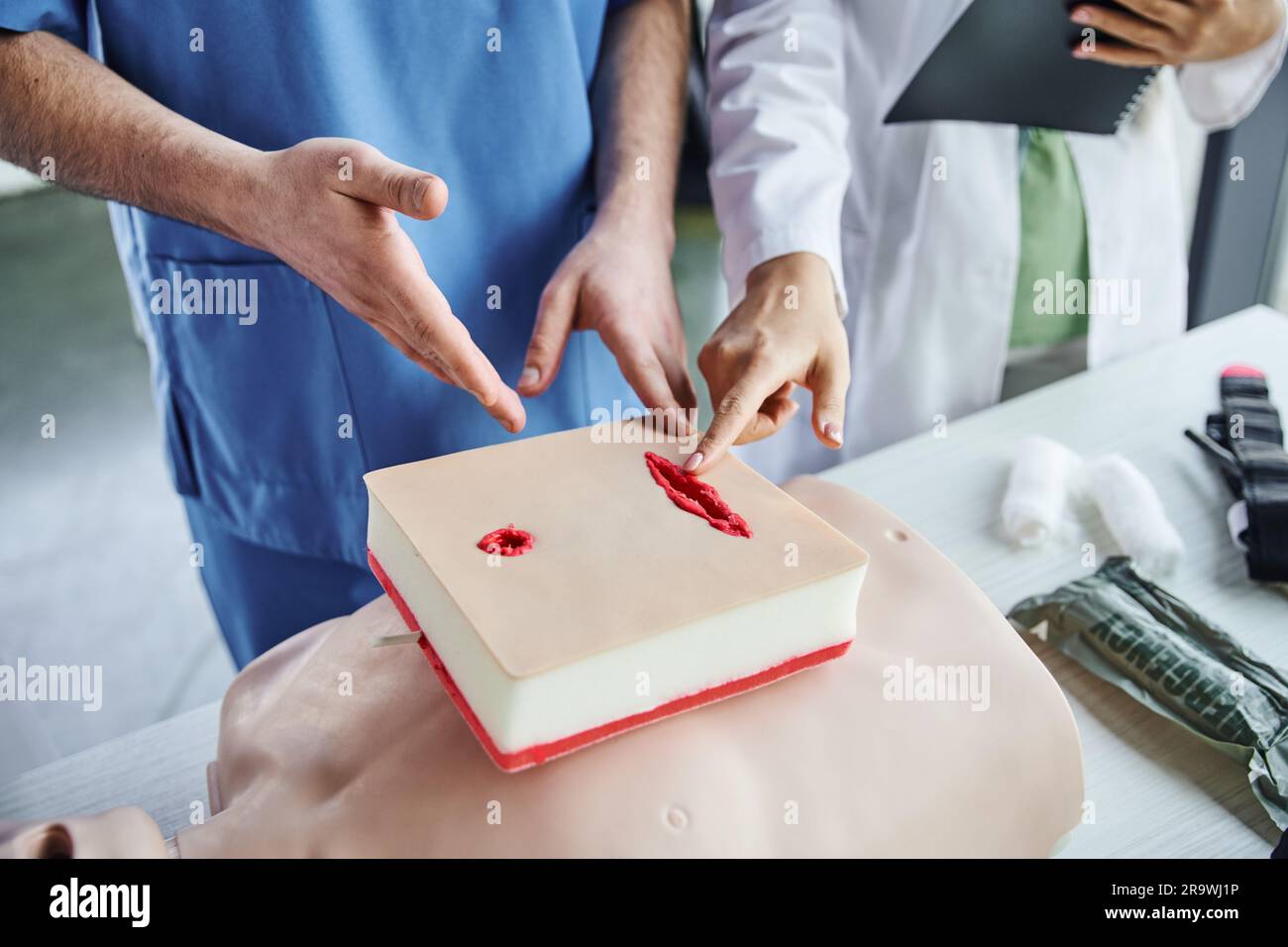 medical seminar, partial view of professional healthcare worker and student pointing at wound care simulator near CPR manikin and bandages, first aid Stock Photo