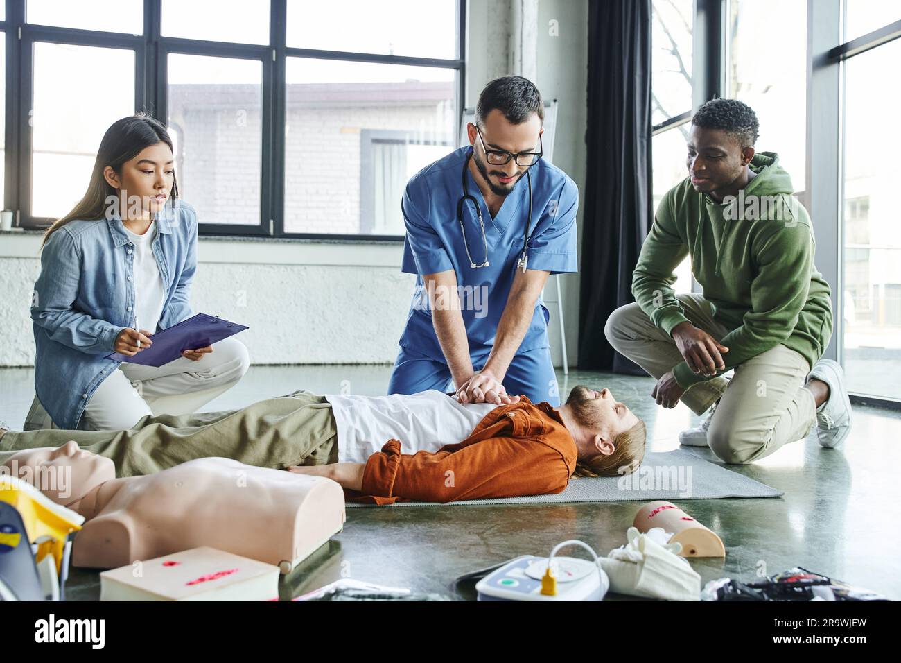 professional paramedic practicing chest compressions on man near CPR manikin, medical equipment and multiethnic participants of first aid training sem Stock Photo