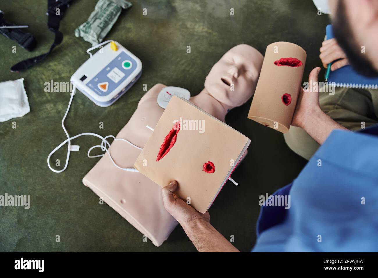 first aid training seminar, cropped view of healthcare worker holding wound care simulators near CPR manikin and automated external defibrillator, saf Stock Photo
