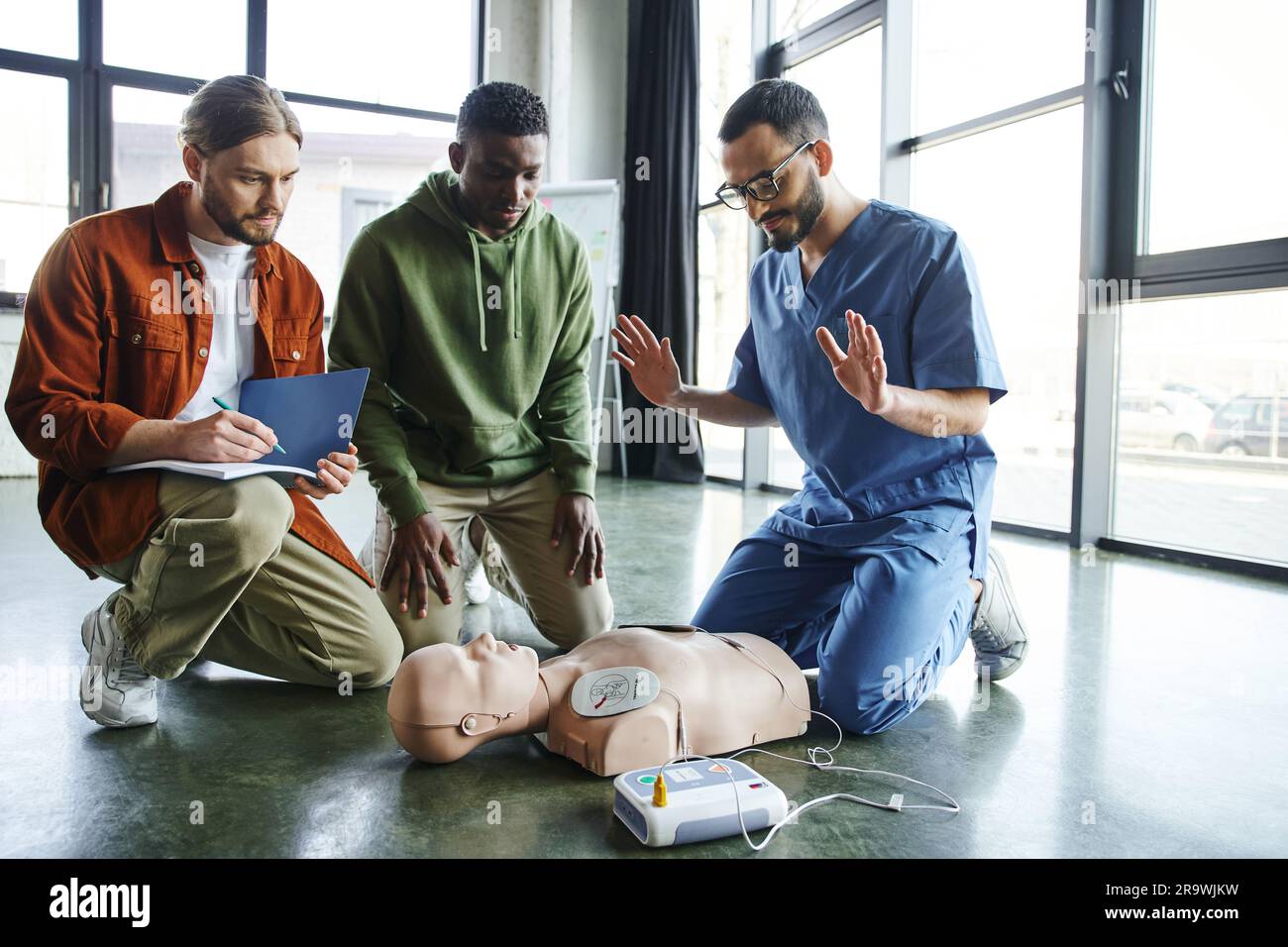 young paramedic explaining cardiac resuscitation techniques to interracial participants near CPR