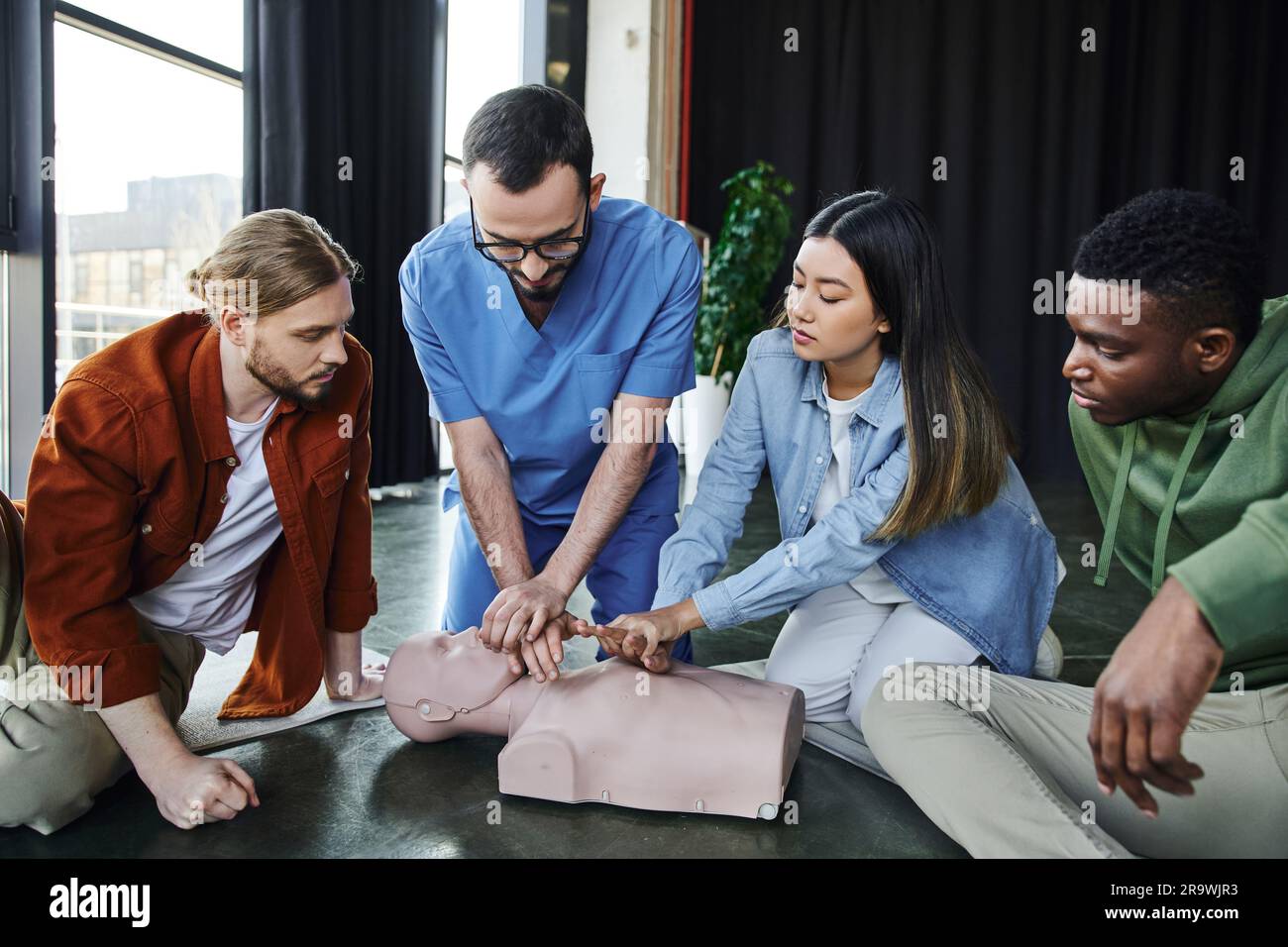 first aid training, medical instructor showing cardiopulmonary resuscitation on CPR manikin near multiethnic participants in training room, effective Stock Photo