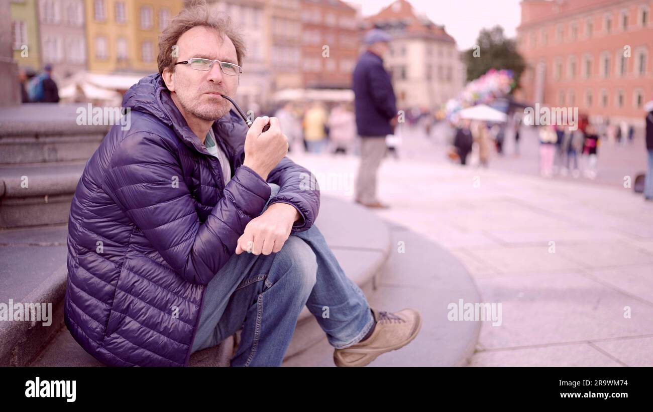 Adult man sitting on square and smoking a tobacco pipe in the Palace Square, Warsaw Old Town Stock Photo