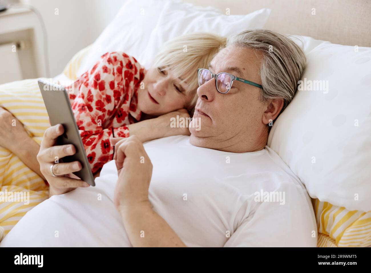 Elderly couple lying together in bed in bedroom looking at smartphone together, Cologne, North Rhine-Westphalia, Germany Stock Photo