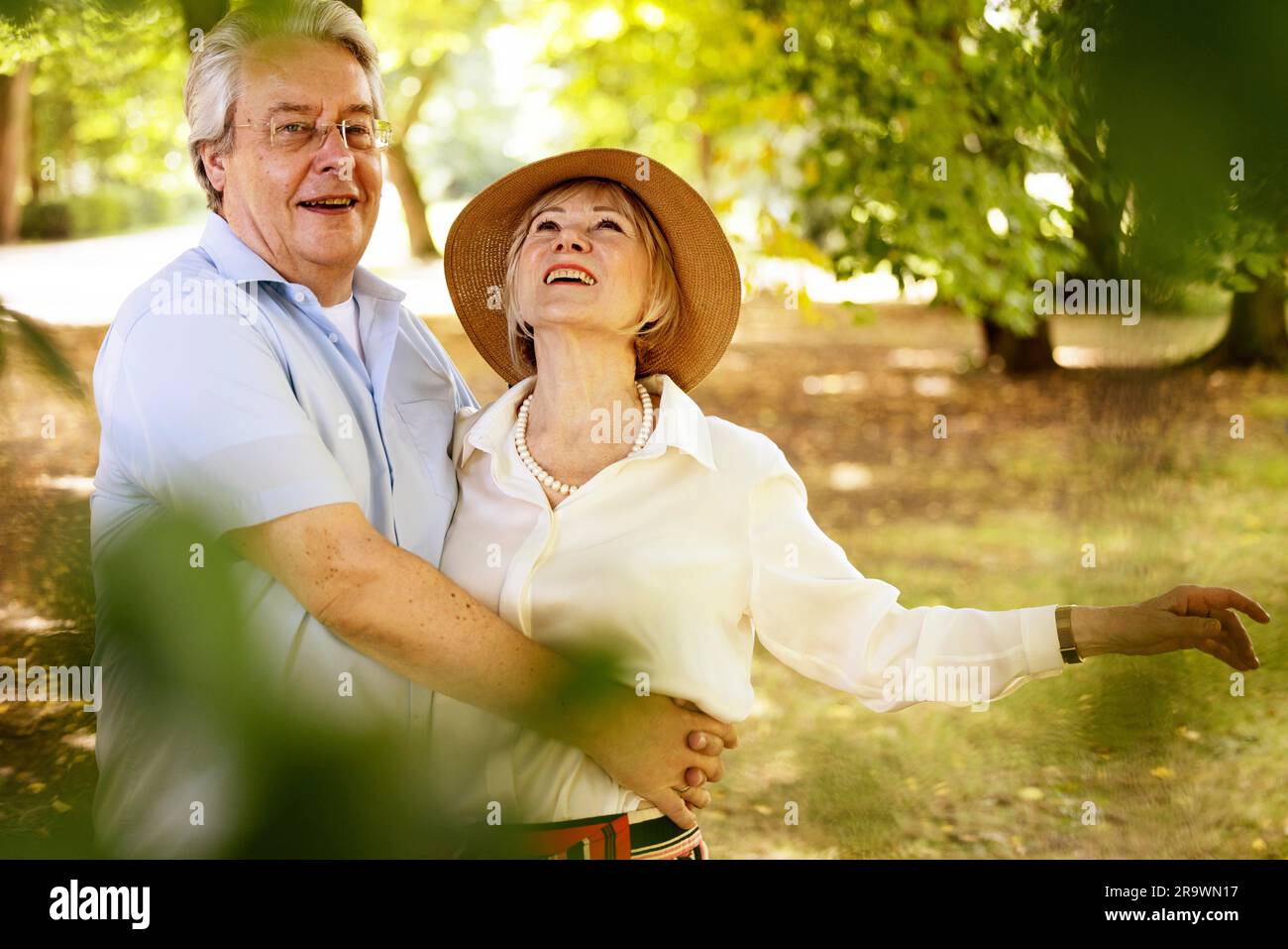 Germany, elderly woman with summer straw hat standing in a park together with her husband, portrait Stock Photo