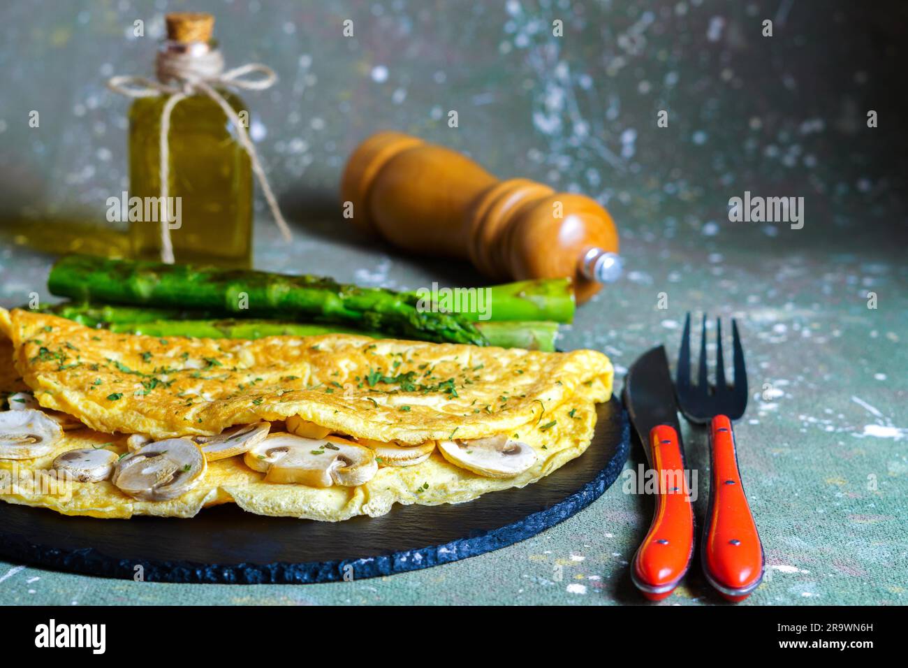 Mushroom omelette with wild asparagus on a slate, with cutlery, pepper and extra virgin olive oil Stock Photo