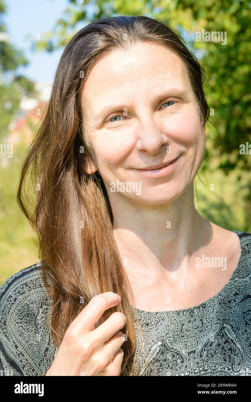 A smiling young senior woman with nice long hair under the summer sun ...