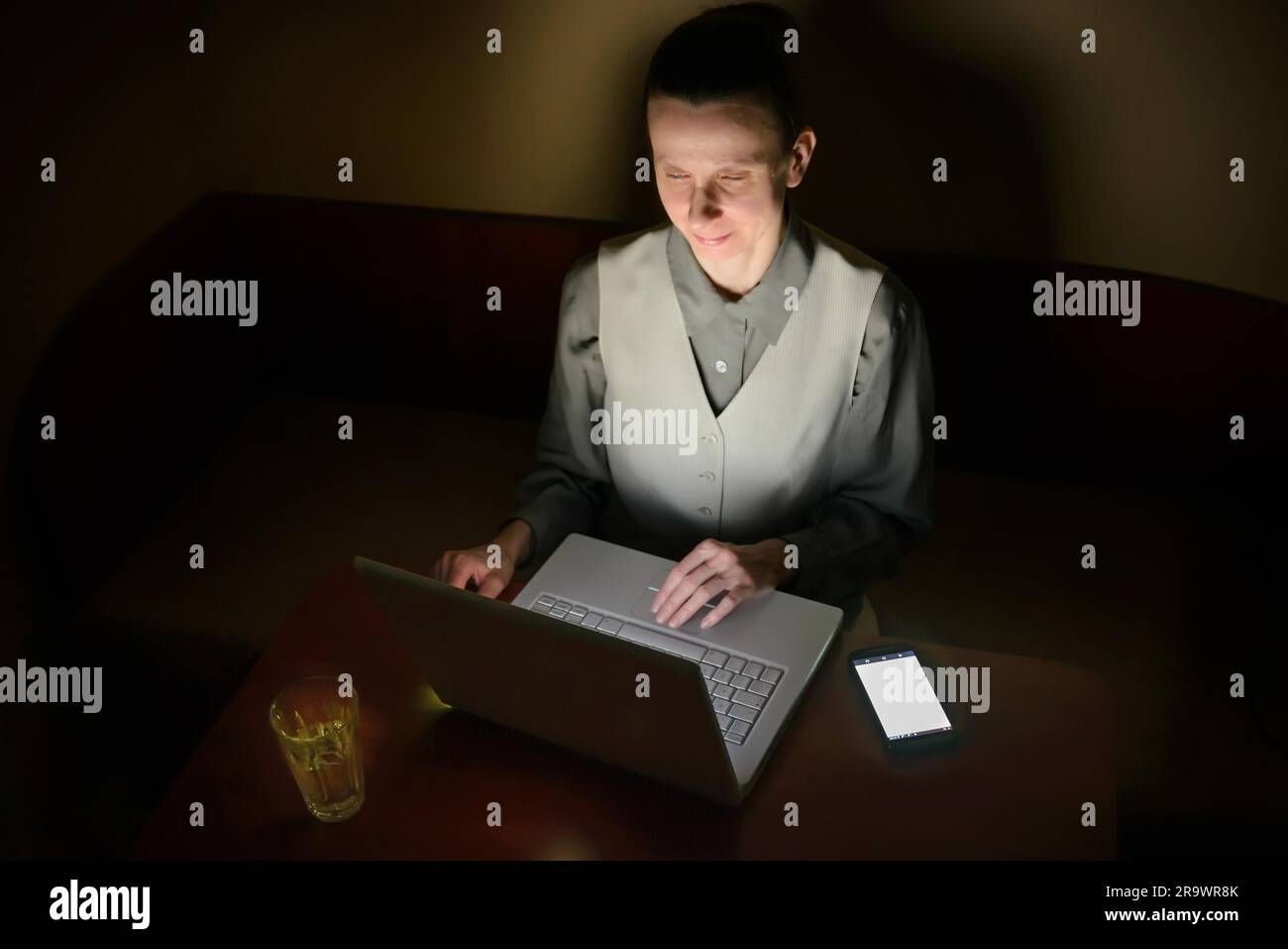 A business woman is using a computer in a dark room. Her face is