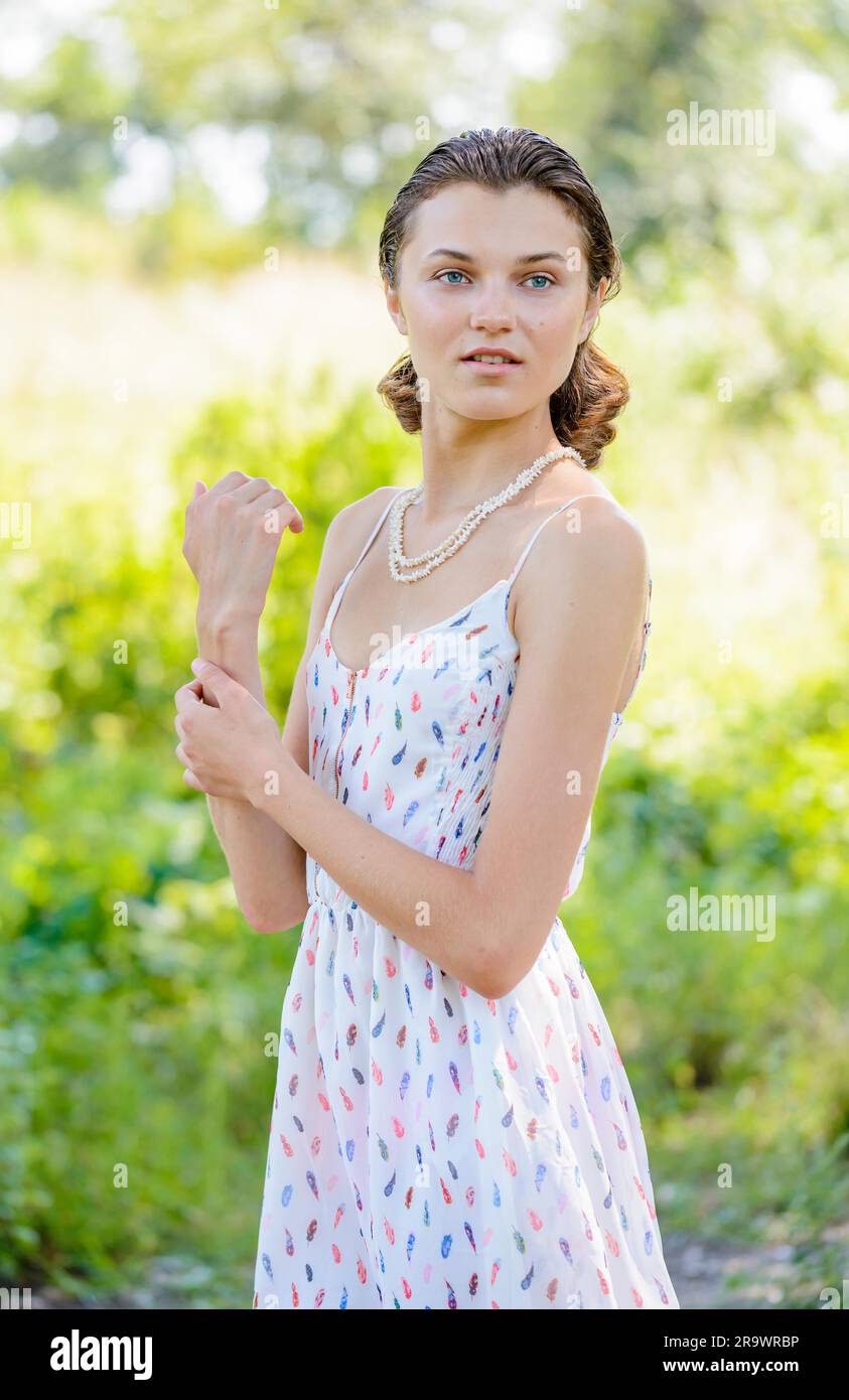 A young woman smiling in the park, with summer back light and trees in the background Stock Photo