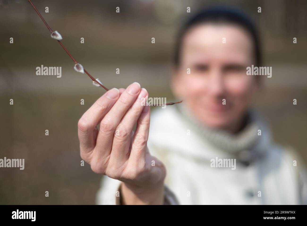 A woman is holding a willow branch in her hand and looking a catkin at the beginning of spring Stock Photo
