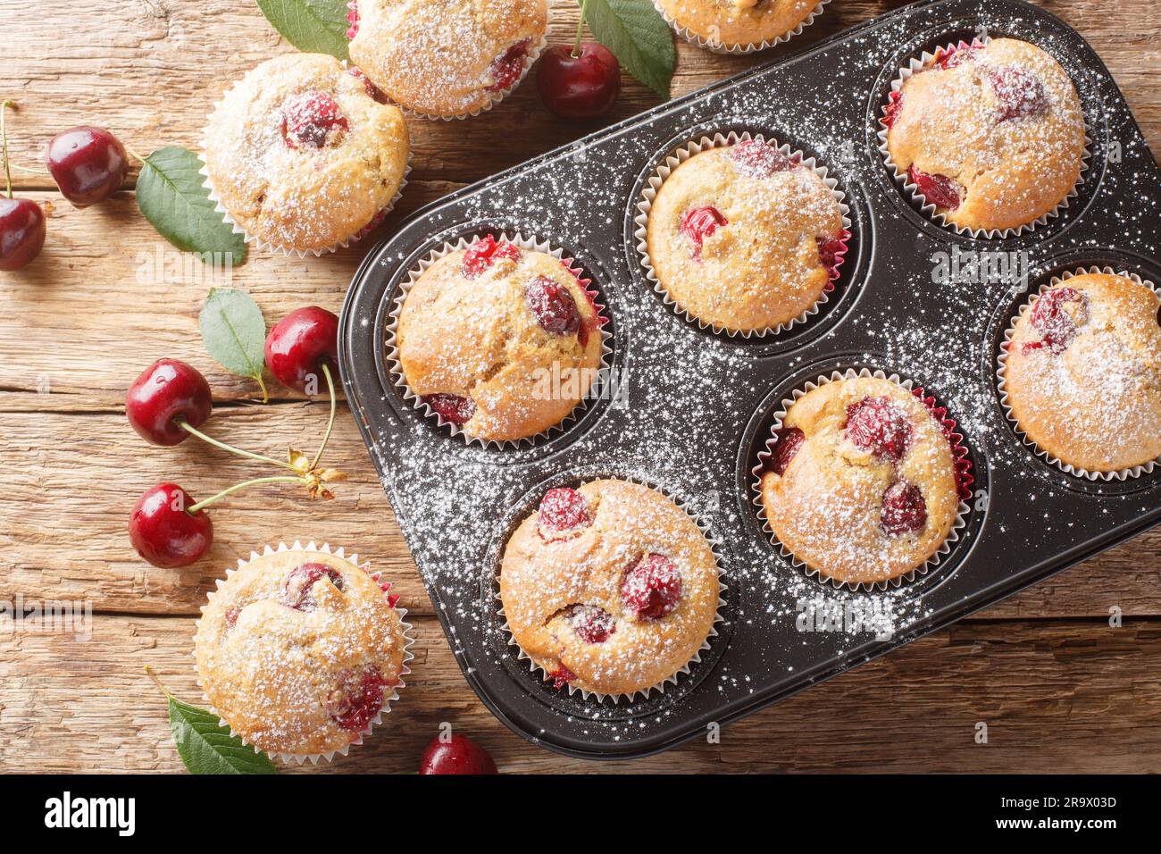Homemade sweet and sour muffins with fresh cherries close-up in a muffin tin on the table. Horizontal top view from above Stock Photo