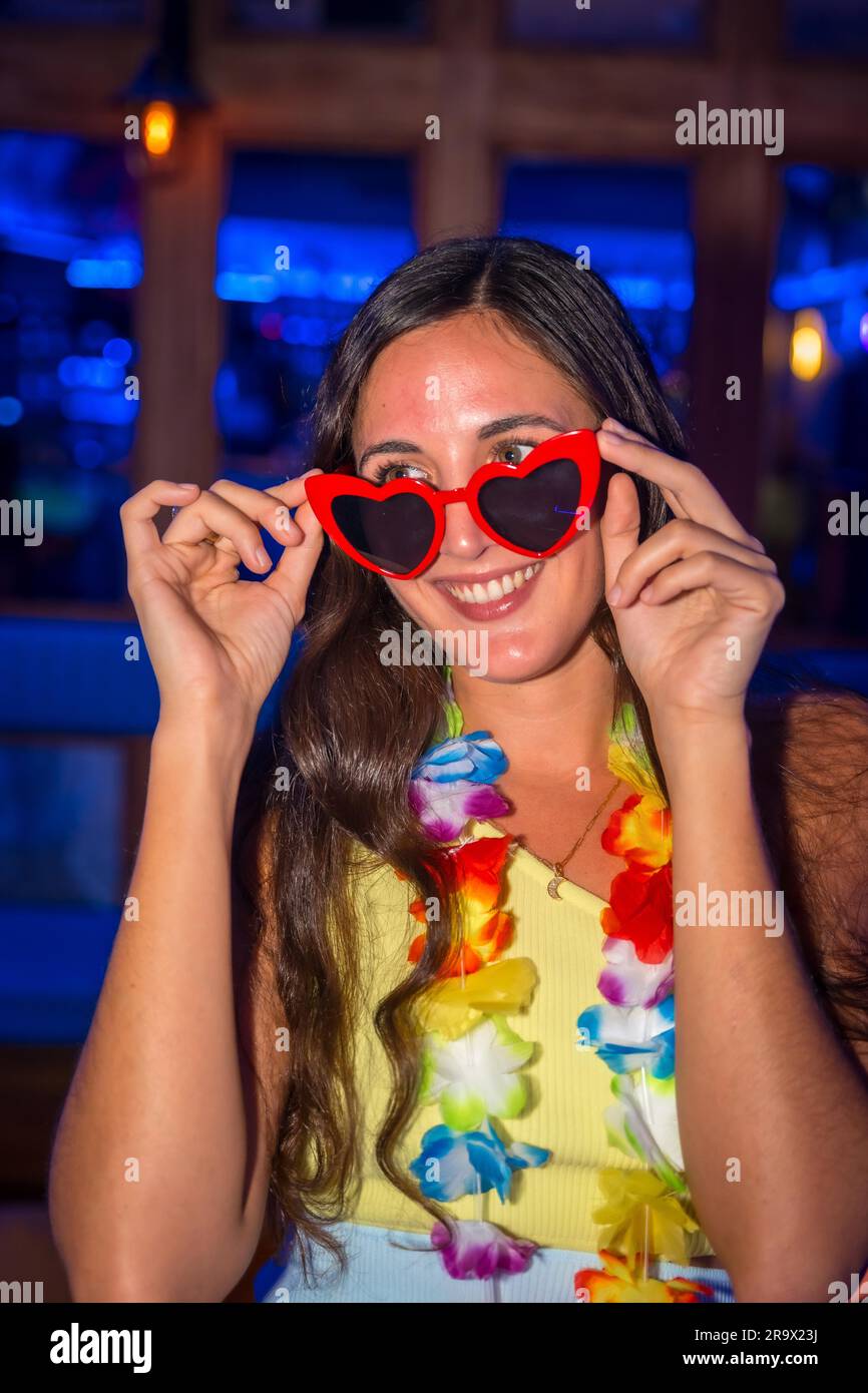 Portrait of attractive latin woman smiling at a night party in a disco with hearts glasses Stock Photo