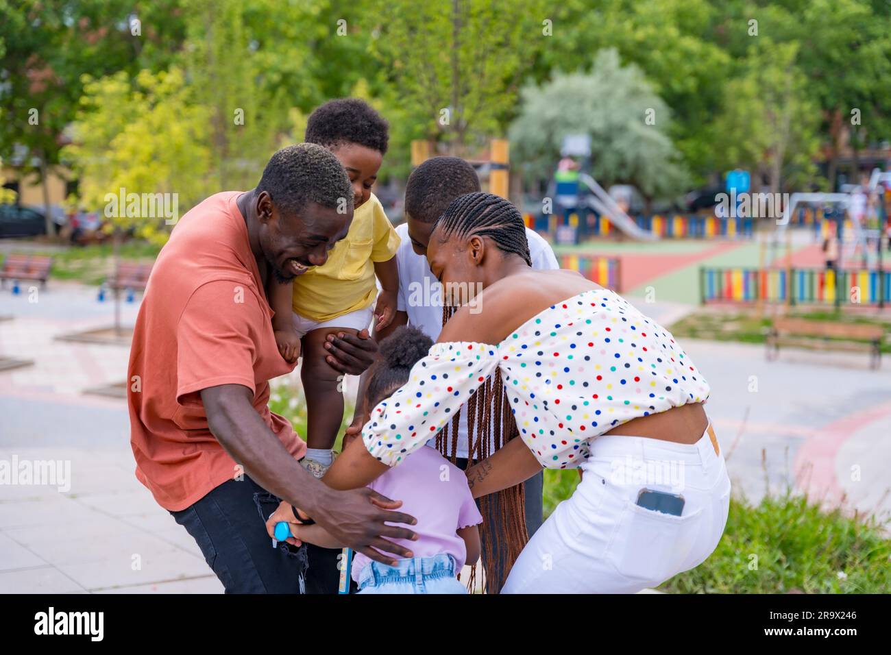 African black ethnic family with children in playground, hugging with bicycle Stock Photo