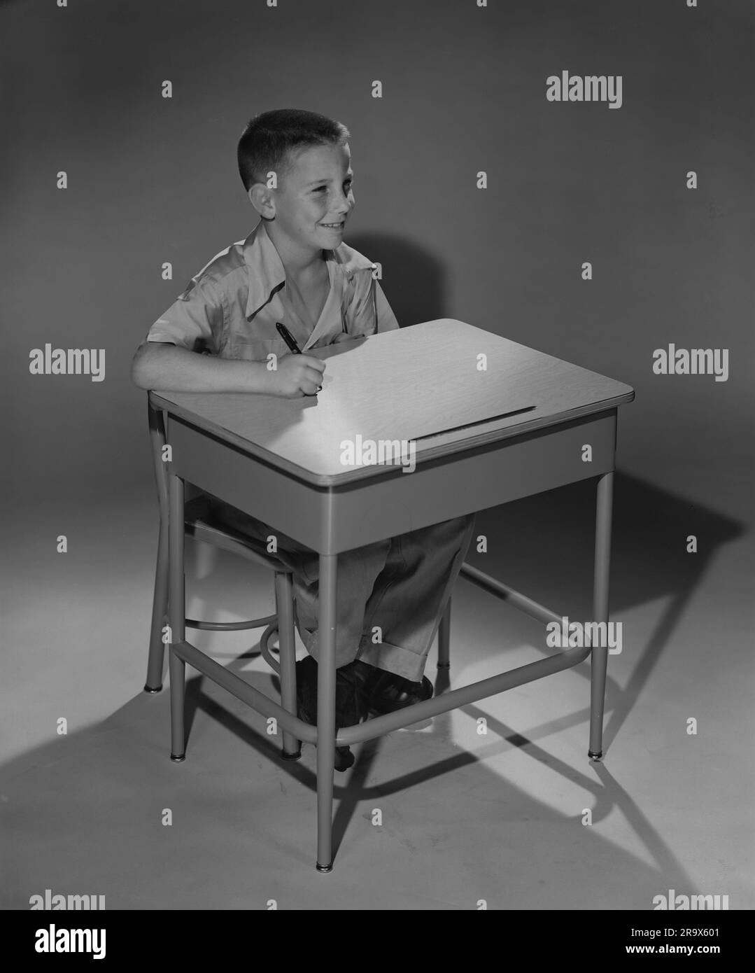 Elementary age boy sitting at his desk with pen in hand, staring straight ahead Stock Photo