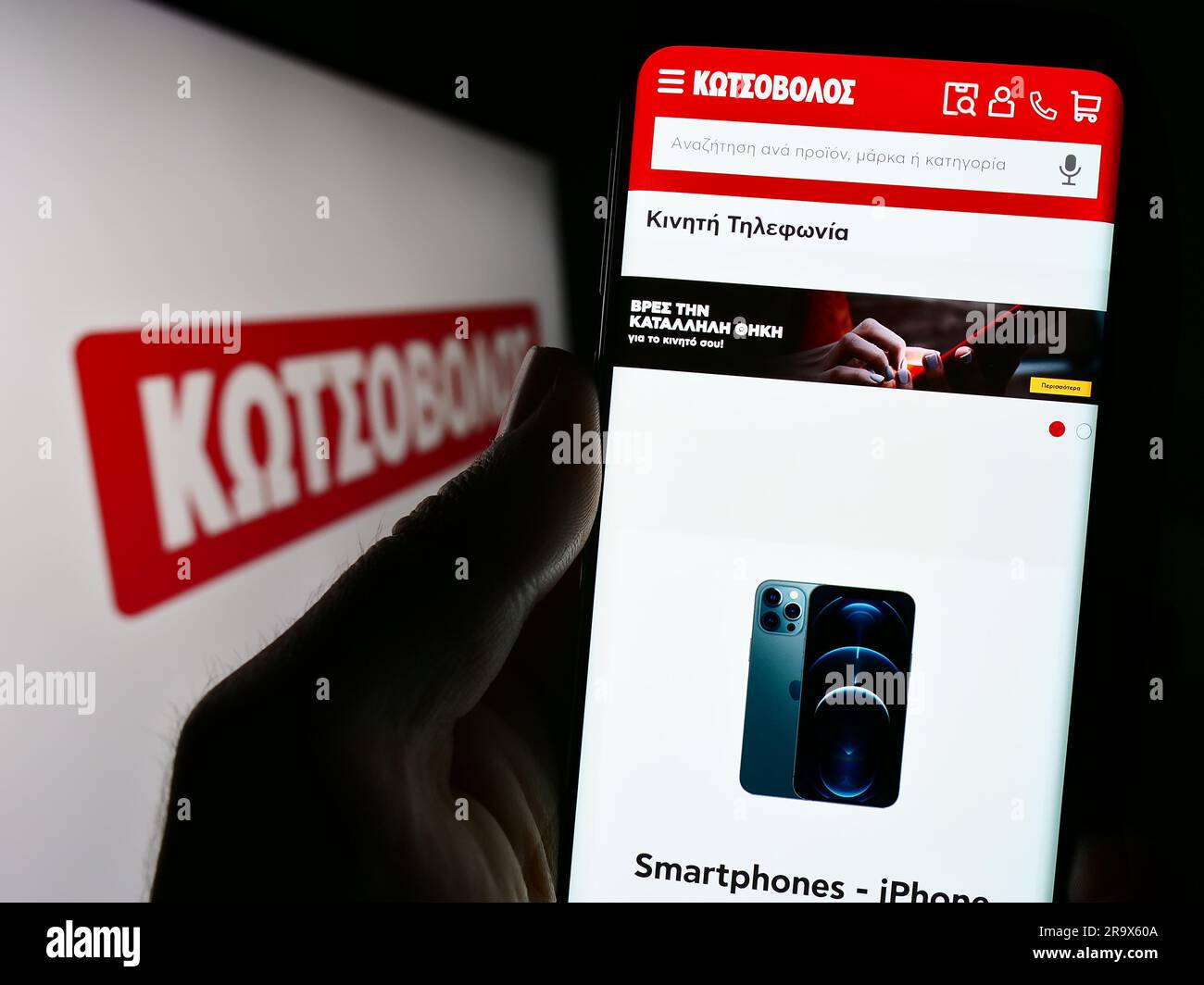 Person holding smartphone with webpage of Greek electronics retail company Kotsovolos on screen with logo. Focus on center of phone display. Stock Photo