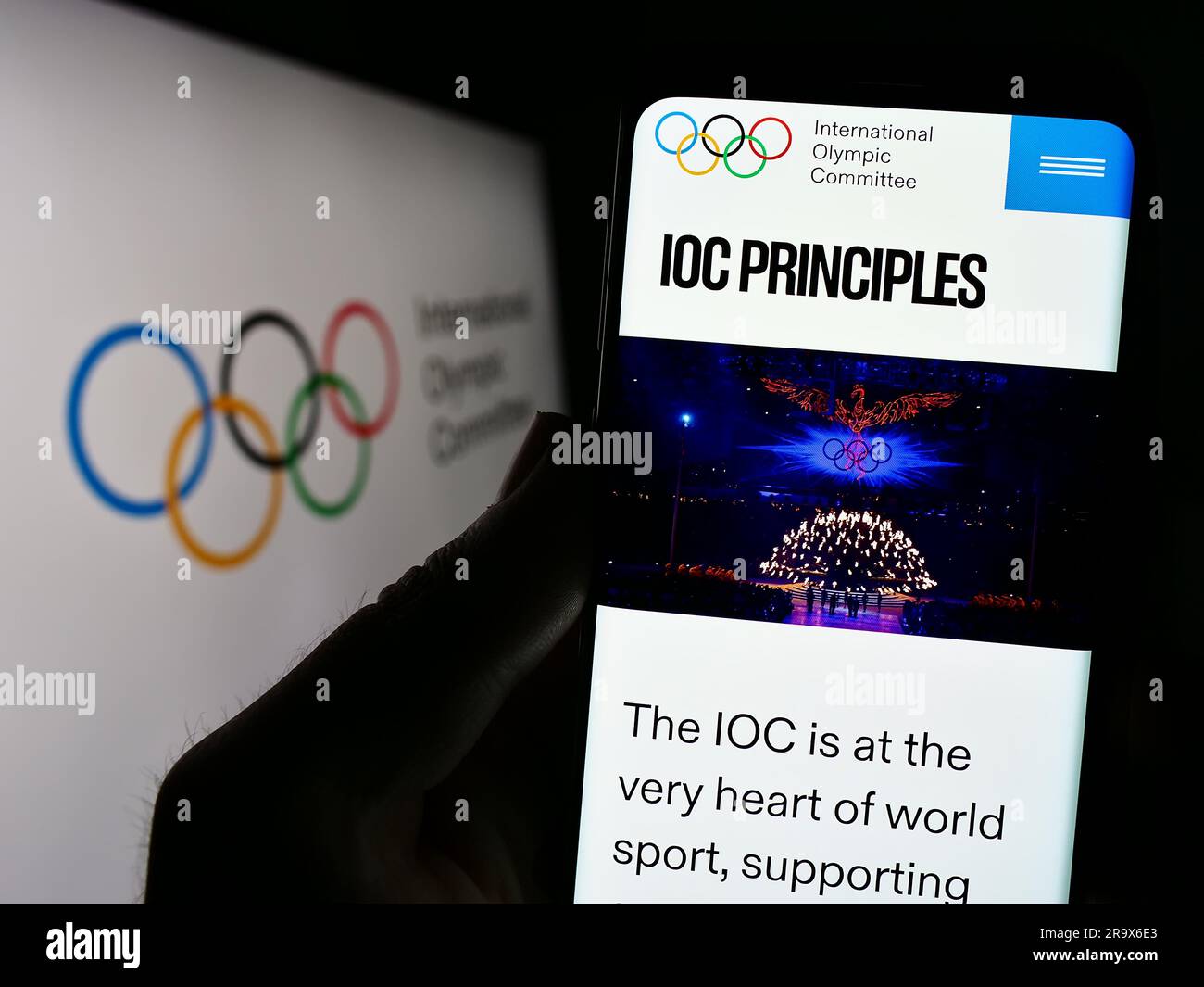 Person holding cellphone with webpage of the International Olympic Committee (IOC) on screen in front of logo. Focus on center of phone display. Stock Photo