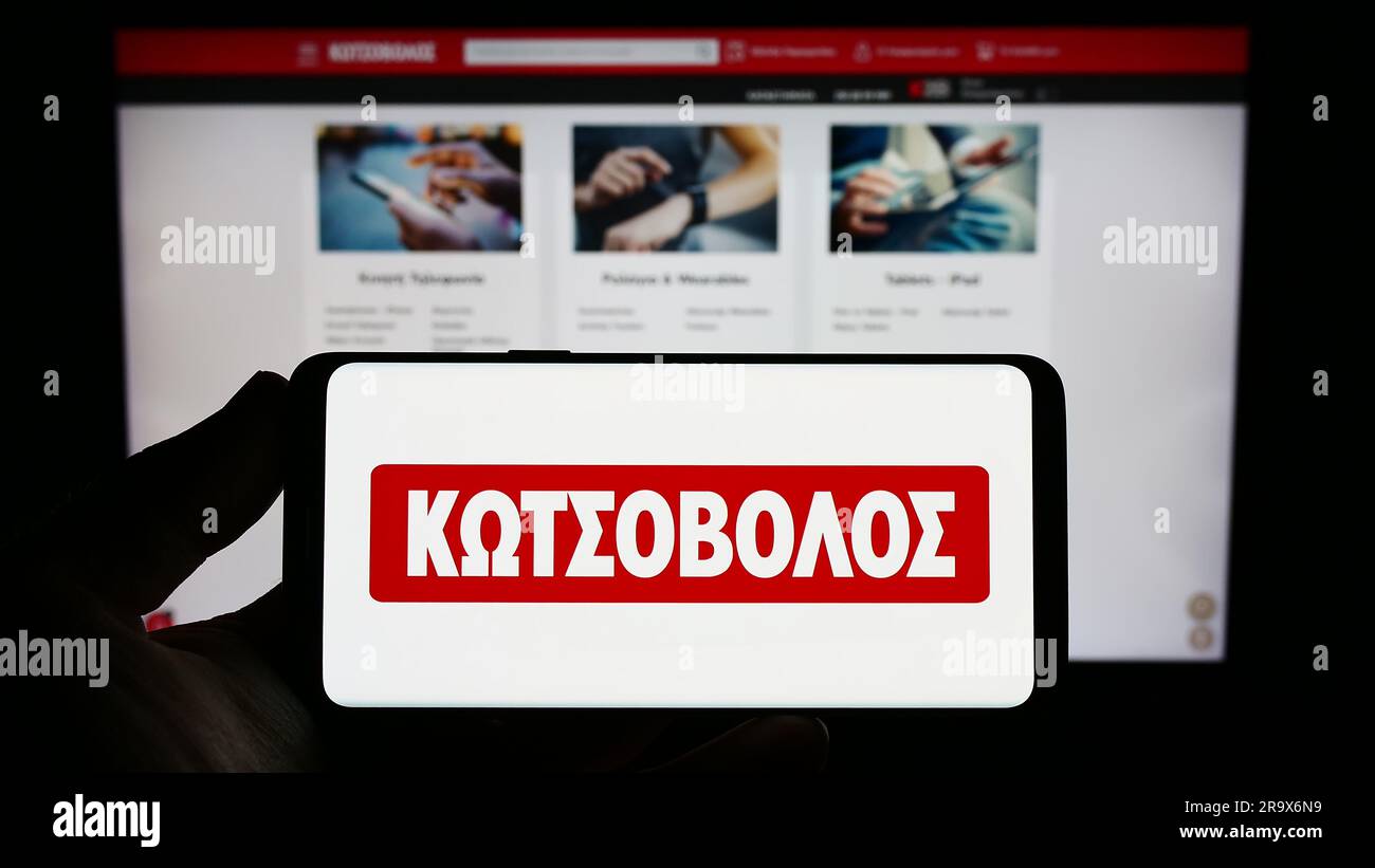Person holding smartphone with logo of Greek electronics retail company Kotsovolos on screen in front of website. Focus on phone display. Stock Photo