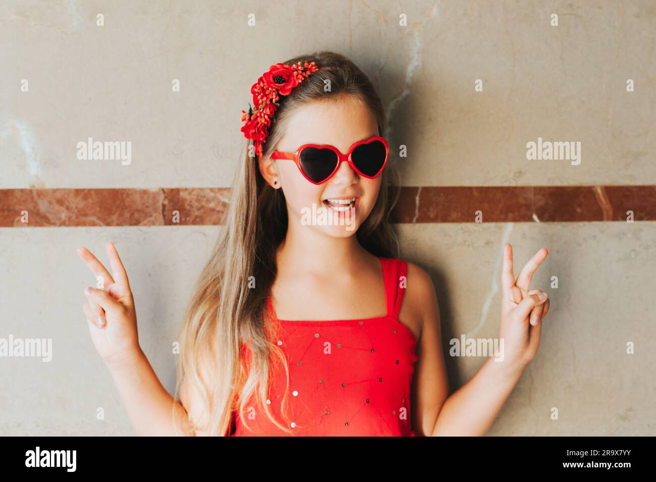 Funny portrait of pretty little girl wearing red dress and heart shaped sunglasses Stock Photo