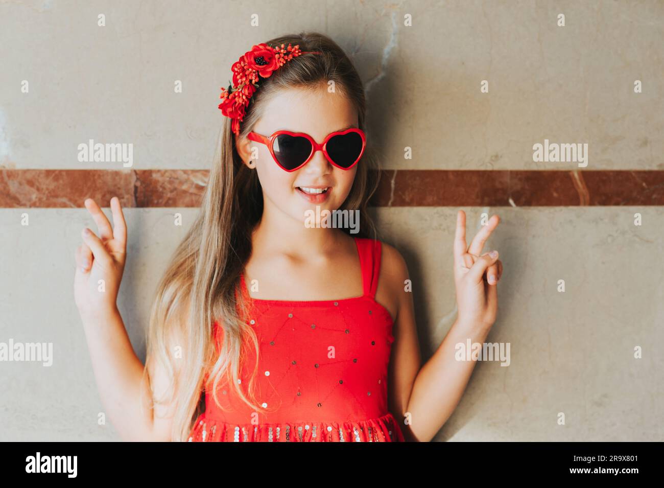 Funny portrait of pretty little girl wearing red dress and heart shaped sunglasses Stock Photo