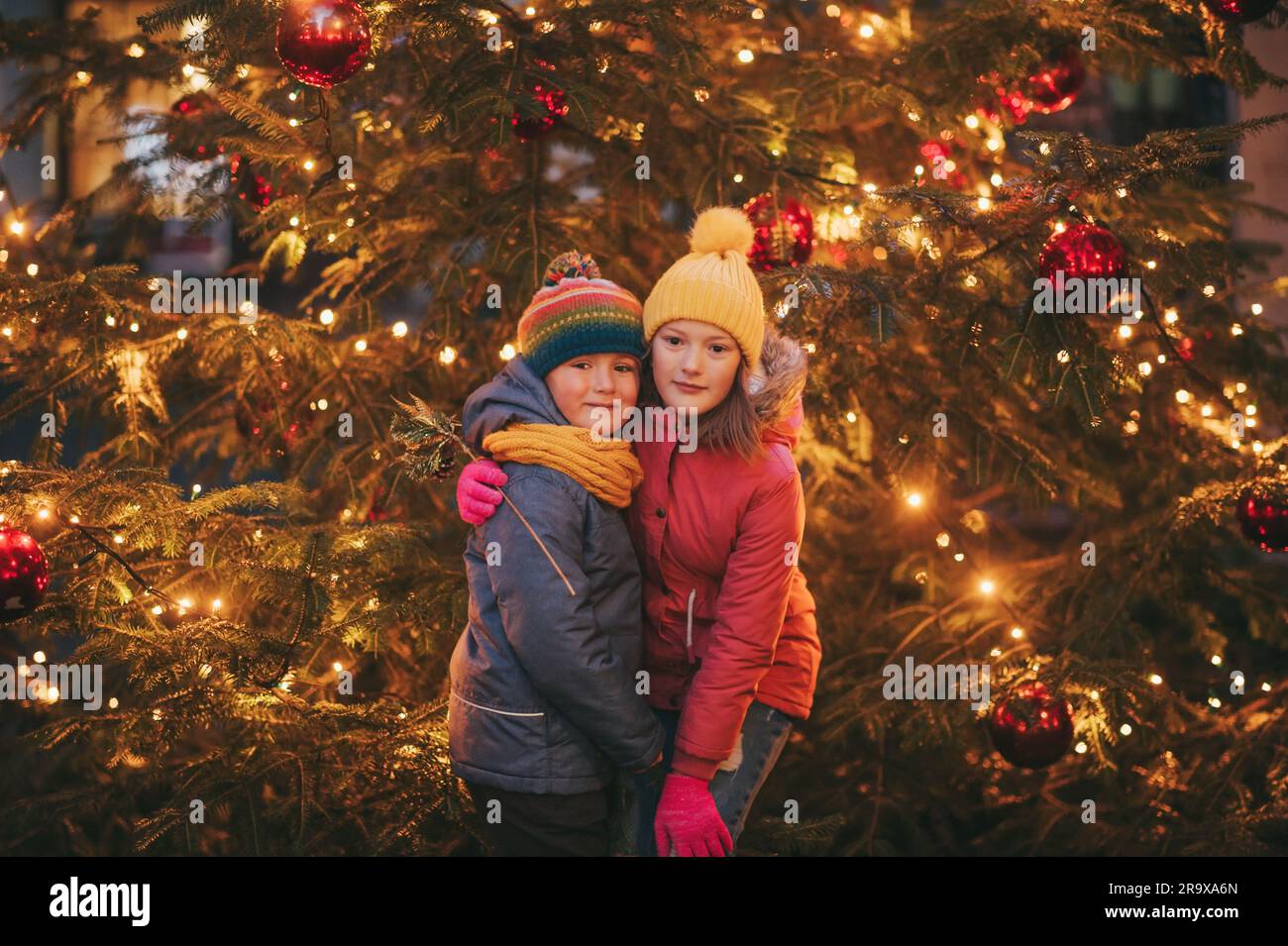 Outdoor portrait of little children next to Christmas tree with lights