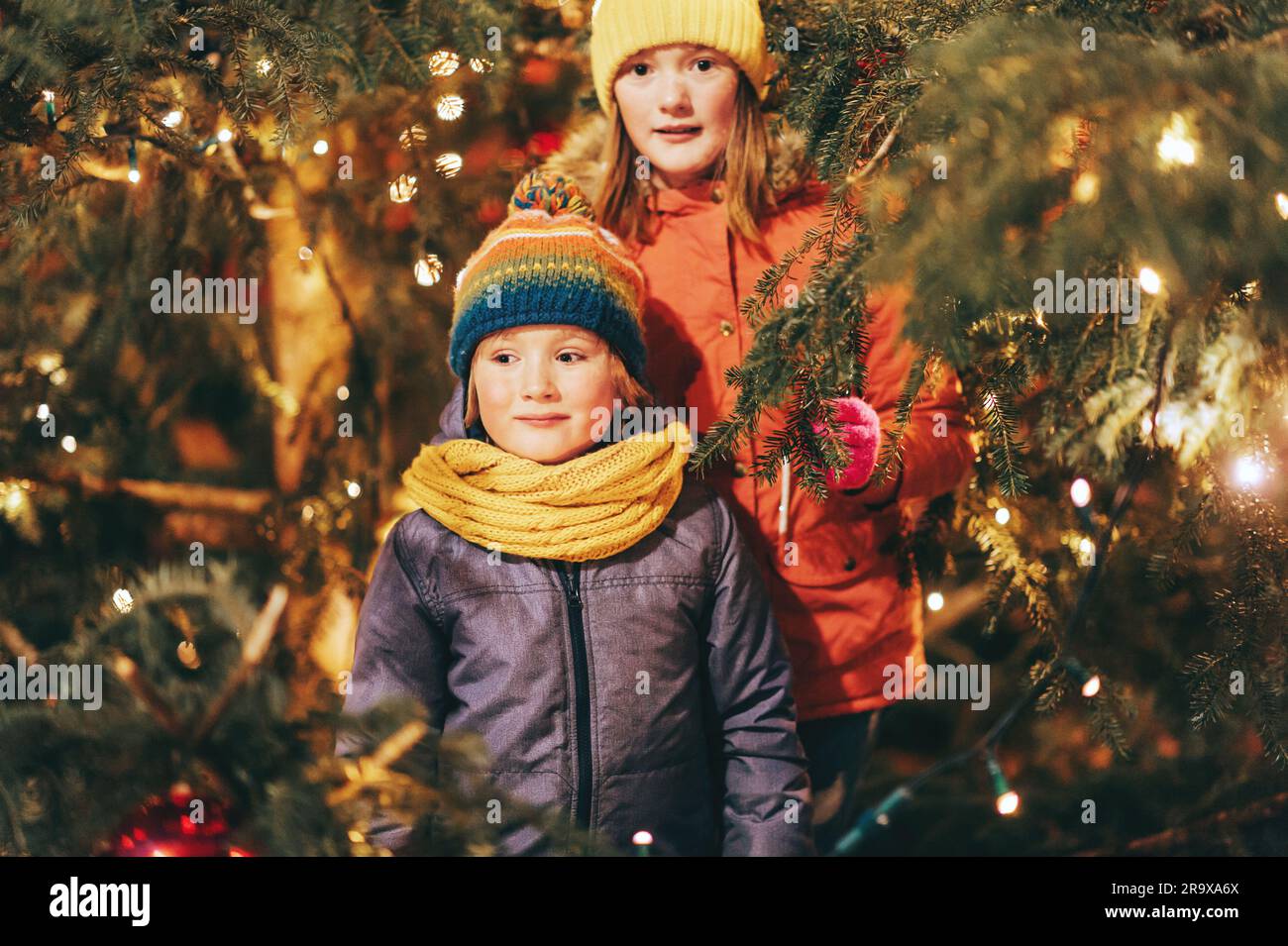 Outdoor portrait of little children next to Christmas tree with lights