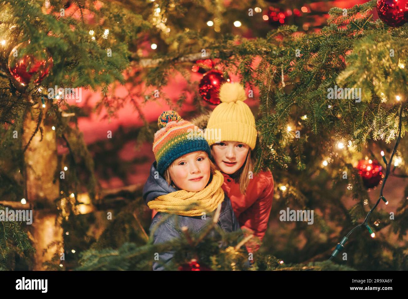 Outdoor portrait of little children next to Christmas tree with lights