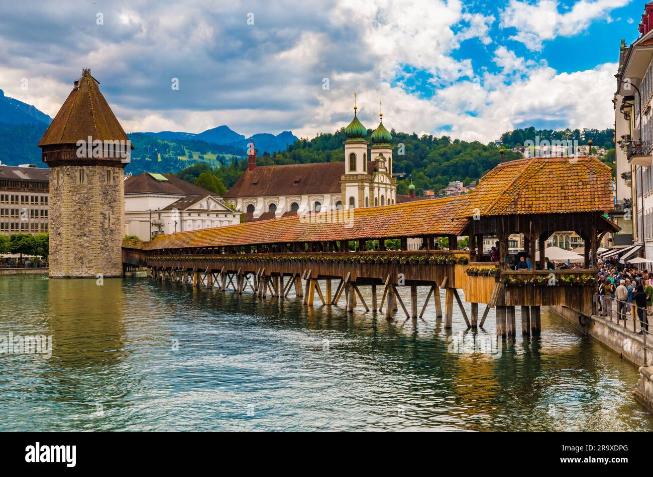 The famous covered timber footbridge Kapellbrücke (Chapel Bridge) with Water Tower over the river Reuss at the street Rathausquai. The Jesuit Church... Stock Photo