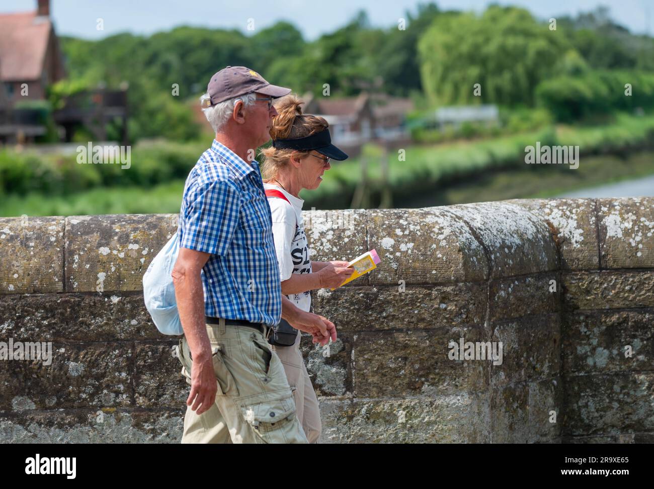 A couple of people walking across a bridge, one looking at a paper map, presumably tourists visiting a British town in England, UK. Stock Photo