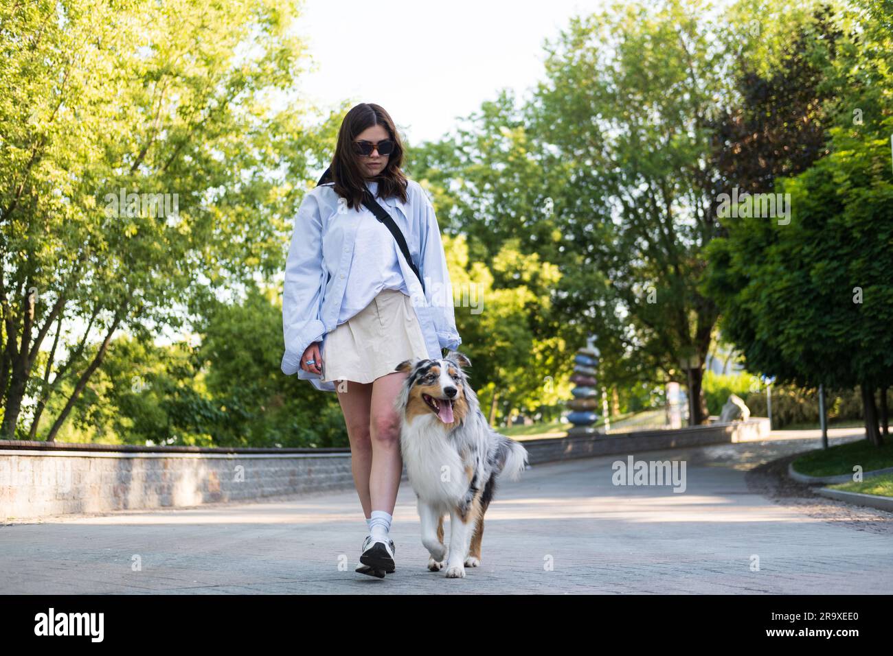 Young woman walking her aussie dog in an urban alley, spending time with pets outdoors. Mid 20s girl with australian shepherd dog on the leash Stock Photo