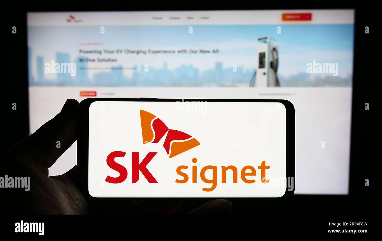 Person holding smartphone with logo of Korean EV charging company SK Signet on screen in front of website. Focus on phone display. Stock Photo