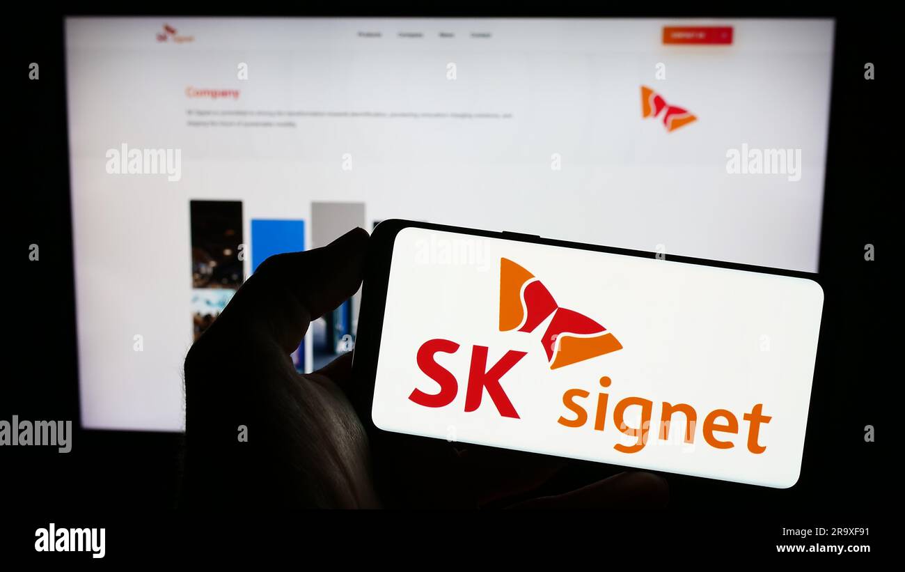 Person holding cellphone with logo of Korean EV charging company SK Signet on screen in front of business webpage. Focus on phone display. Stock Photo