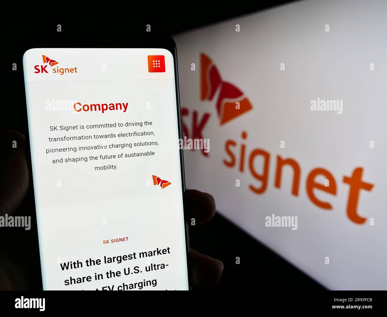 Person holding cellphone with webpage of Korean EV charging company SK Signet on screen in front of logo. Focus on center of phone display. Stock Photo