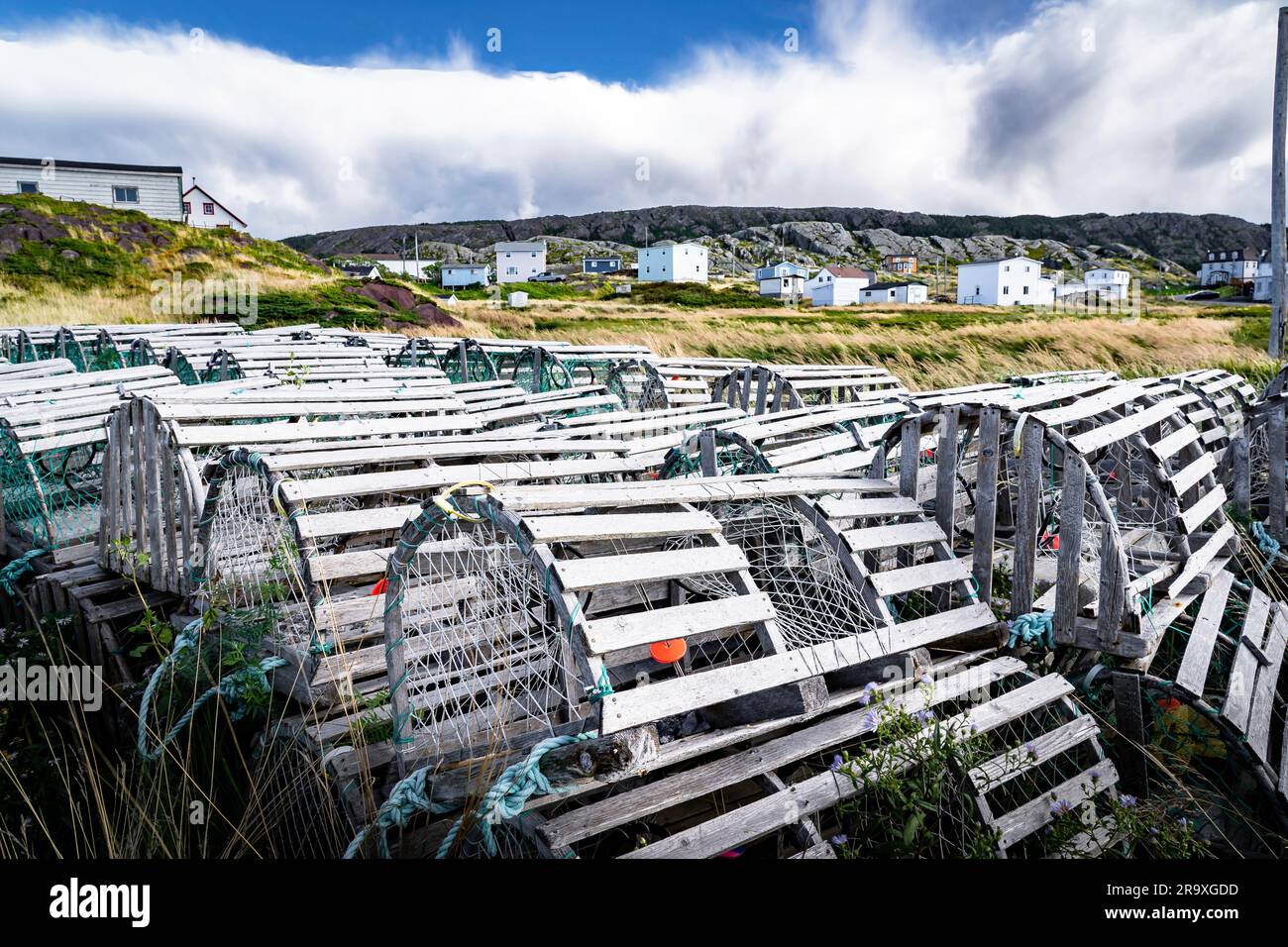 Wooden traditional lobster traps stacked on a shoreline overlooking small rustic homes along the East coast of Canada in Keels Newfoundland and Labrad Stock Photo